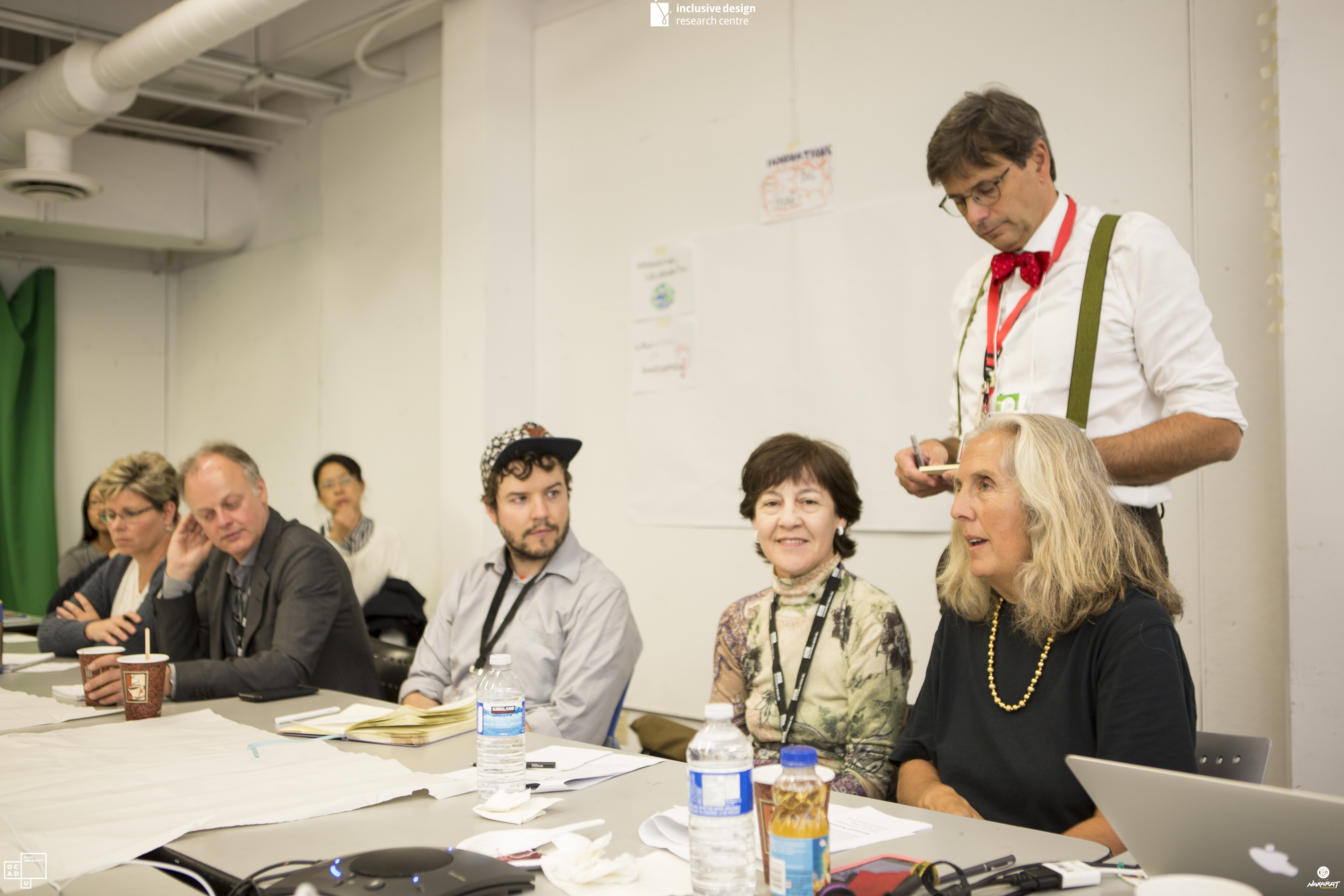 Eight people at a conference table listening to a speaker on the right